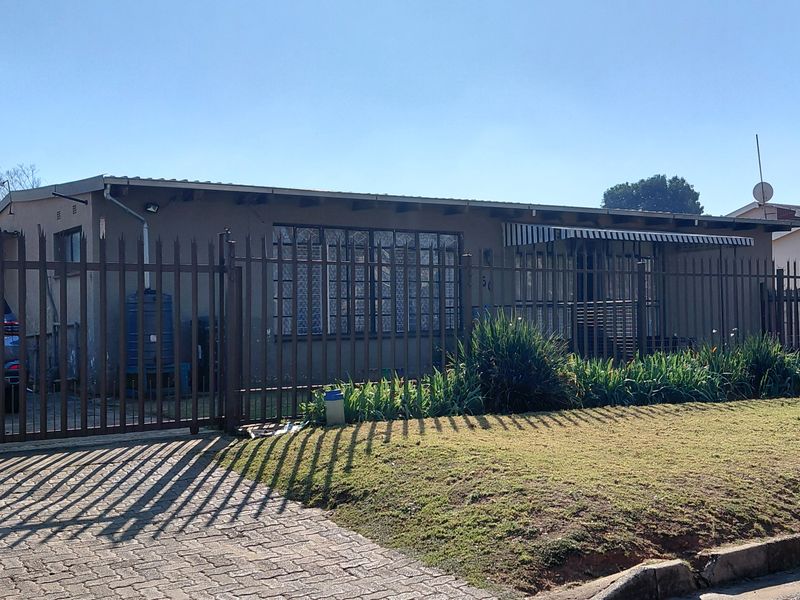 Front elevation of a single-story house featuring a paved driveway, security fencing, and security gates.