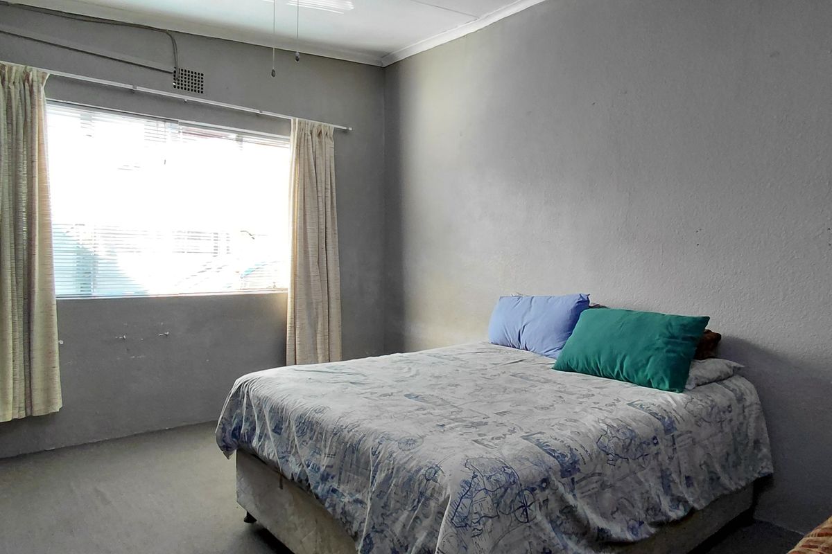 A bedroom featuring built-in cupboards, a ceiling fan, and a window with curtain rails, requiring cosmetic updates to the wall finishes.