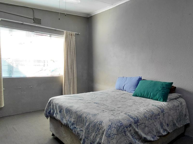 A bedroom featuring built-in cupboards, a ceiling fan, and a window with curtain rails, requiring cosmetic updates to the wall finishes.