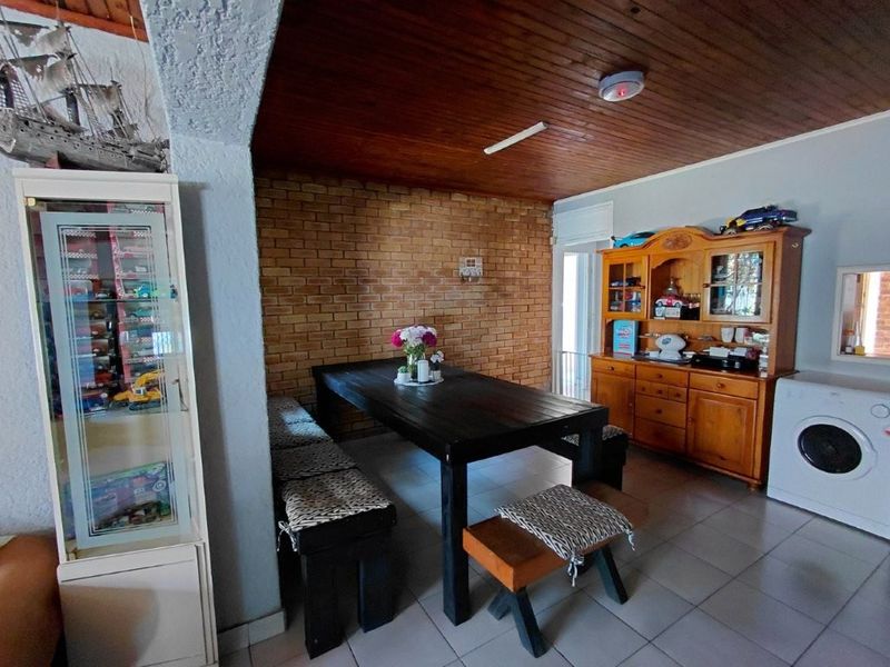 Open plan dining area featuring a rustic exposed brick wall, timber ceiling, and tiled flooring, creating a warm and functional living space.
