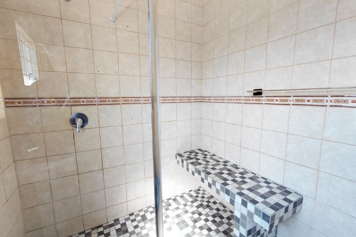 A walk-in shower featuring a built-in tiled bench, glass screen, and overhead shower head, finished with neutral wall tiles and a checkered floor pattern.