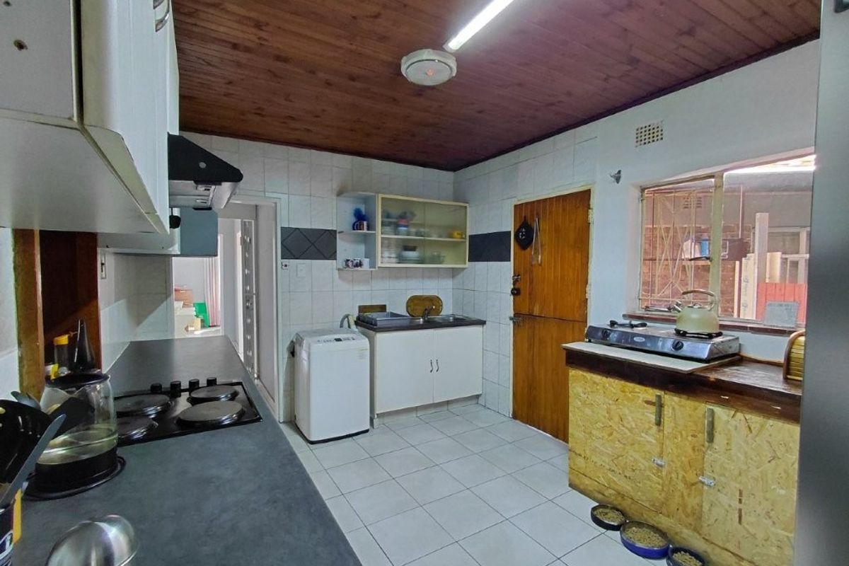 A functional kitchen featuring tiled flooring, timber ceiling, built-in cabinetry, and a hob, offering potential for modernization and aesthetic improvement.