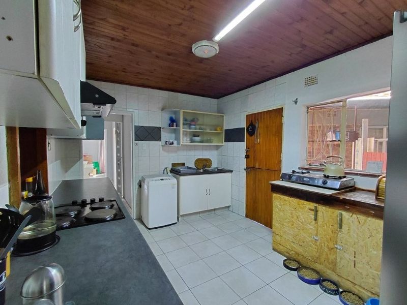 A functional kitchen featuring tiled flooring, timber ceiling, built-in cabinetry, and a hob, offering potential for modernization and aesthetic improvement.