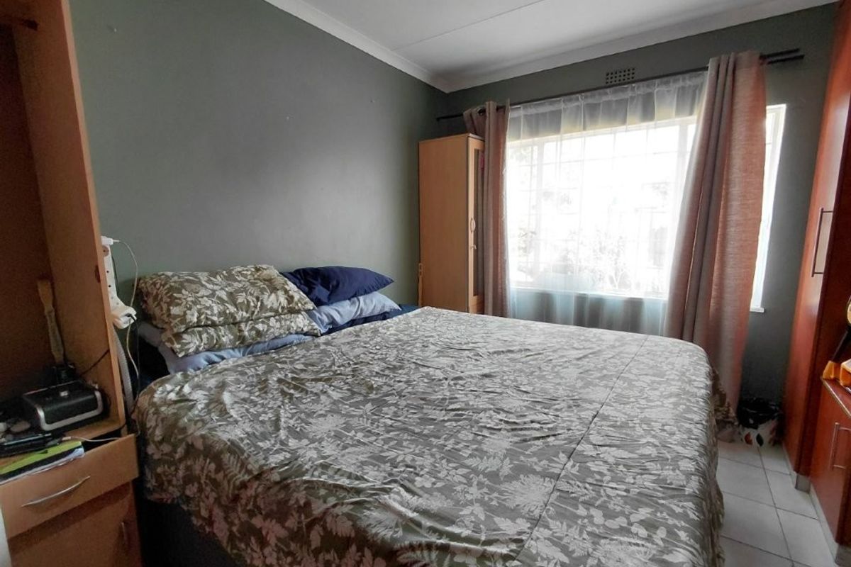 A functional bedroom featuring tiled flooring, cove cornicing, and a window fitted with security bars, providing a practical and well-lit sleeping space.