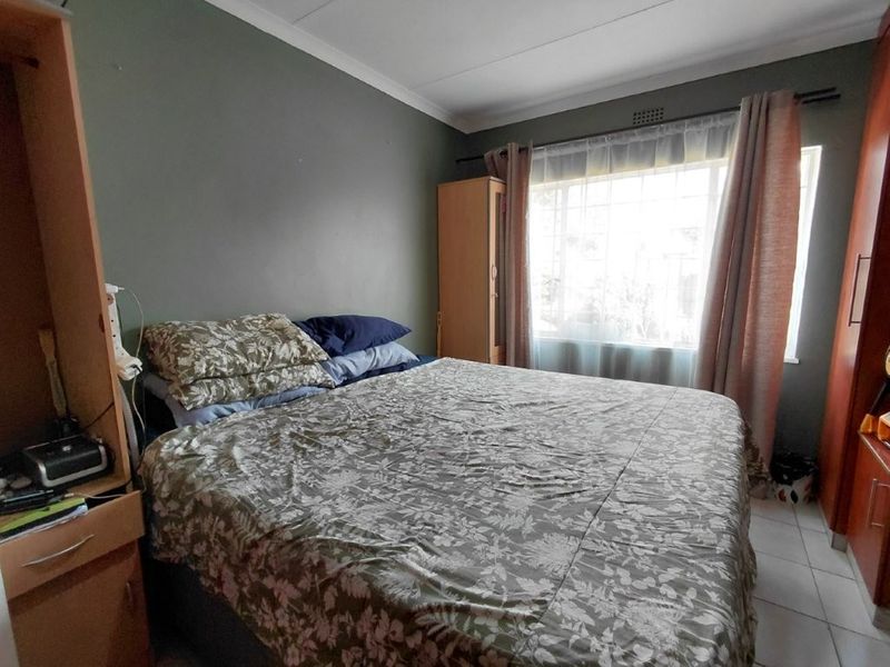 A functional bedroom featuring tiled flooring, cove cornicing, and a window fitted with security bars, providing a practical and well-lit sleeping space.