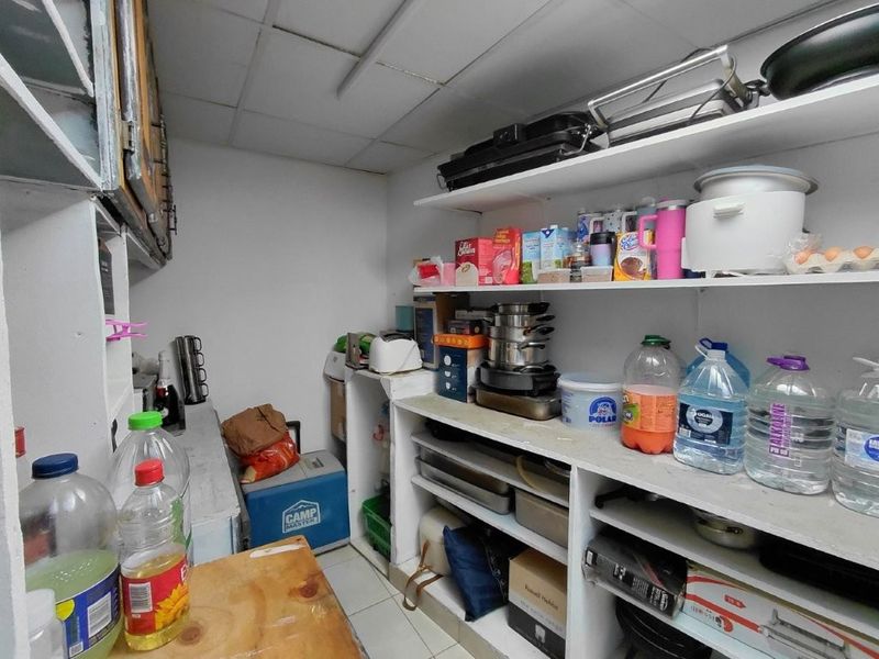 A functional scullery or pantry area featuring extensive built-in shelving and a drop ceiling, providing ample storage space for kitchen essentials.