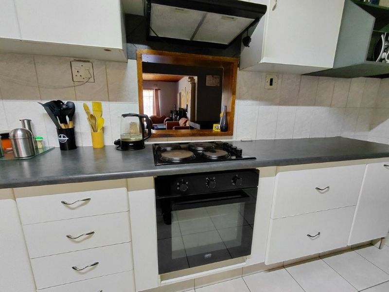 A functional kitchen featuring white cabinetry, dark laminate countertops, a built-in oven, electric hob, and a tiled backsplash with a serving hatch.