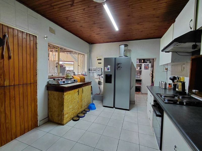 A functional kitchen featuring tiled floors, timber ceiling, built-in cabinetry, and an integrated oven and hob, with an adjacent scullery area.