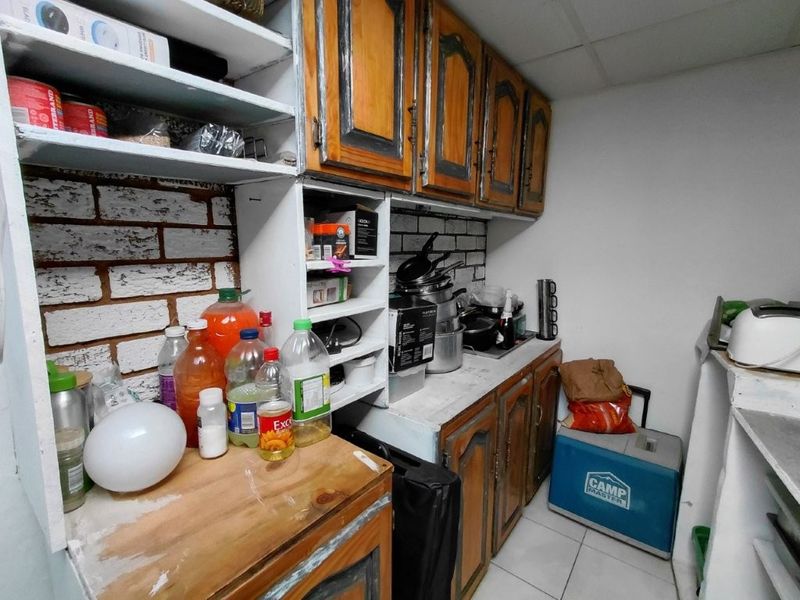 A compact scullery area featuring built-in wooden cabinetry, exposed brick backsplash, and tiled flooring, offering functional storage and prep space.