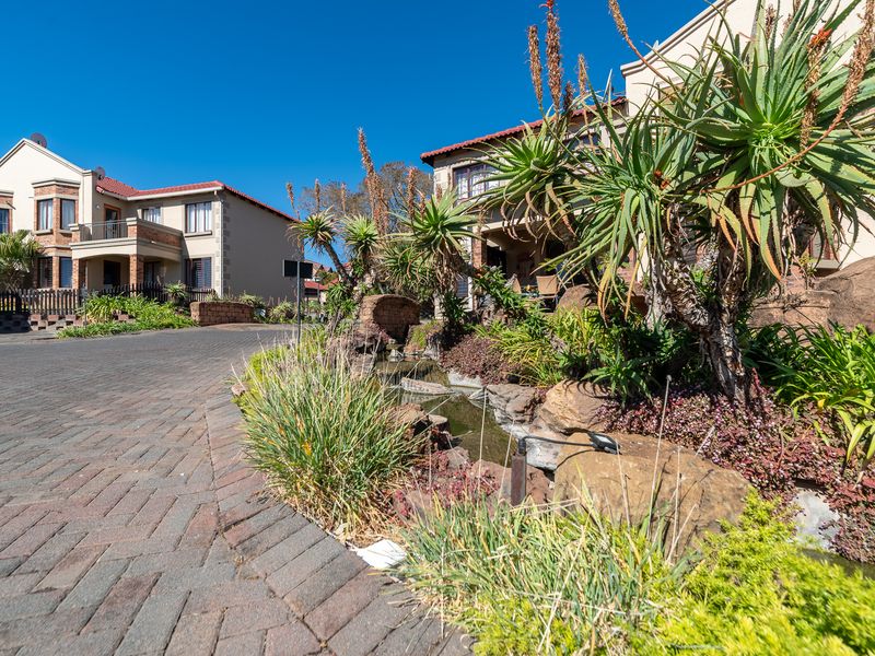 A well-maintained residential complex exterior featuring a paved driveway, landscaped rock garden with a water feature, and classic brick architecture.