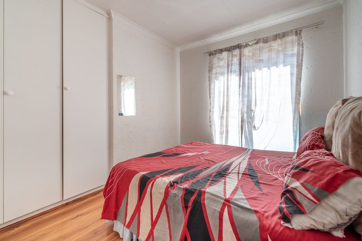 A functional bedroom featuring laminate flooring, built-in cupboards, and a sliding door providing natural light.