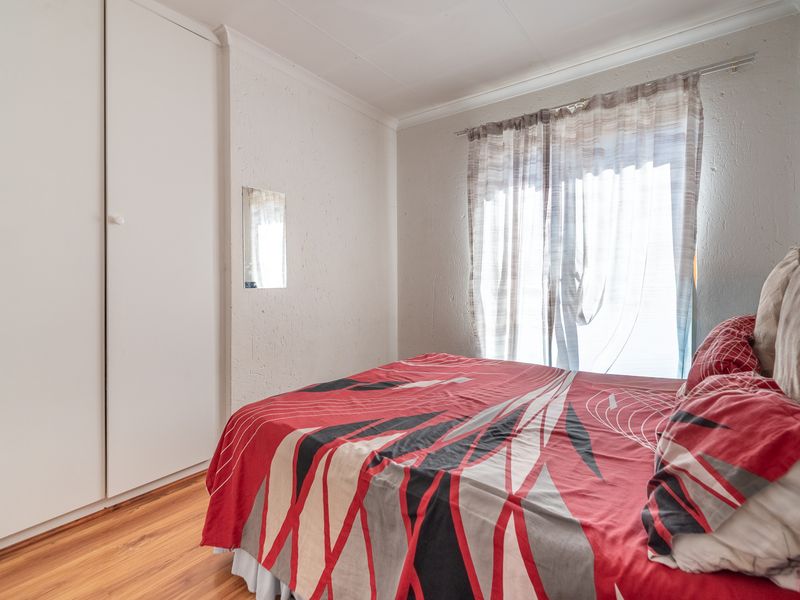 A functional bedroom featuring laminate flooring, built-in cupboards, and a sliding door providing natural light.