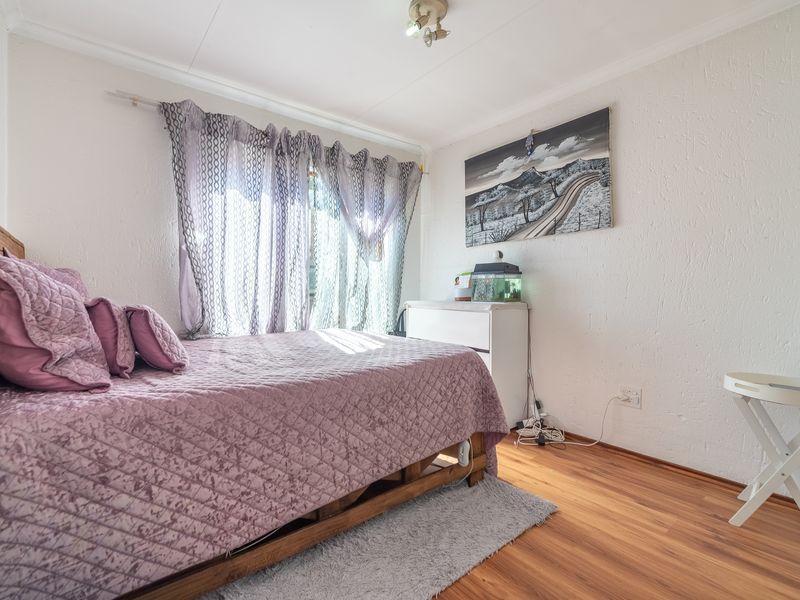 A bedroom featuring laminate flooring, textured walls, and a window with curtain rod, providing a functional space for rest.