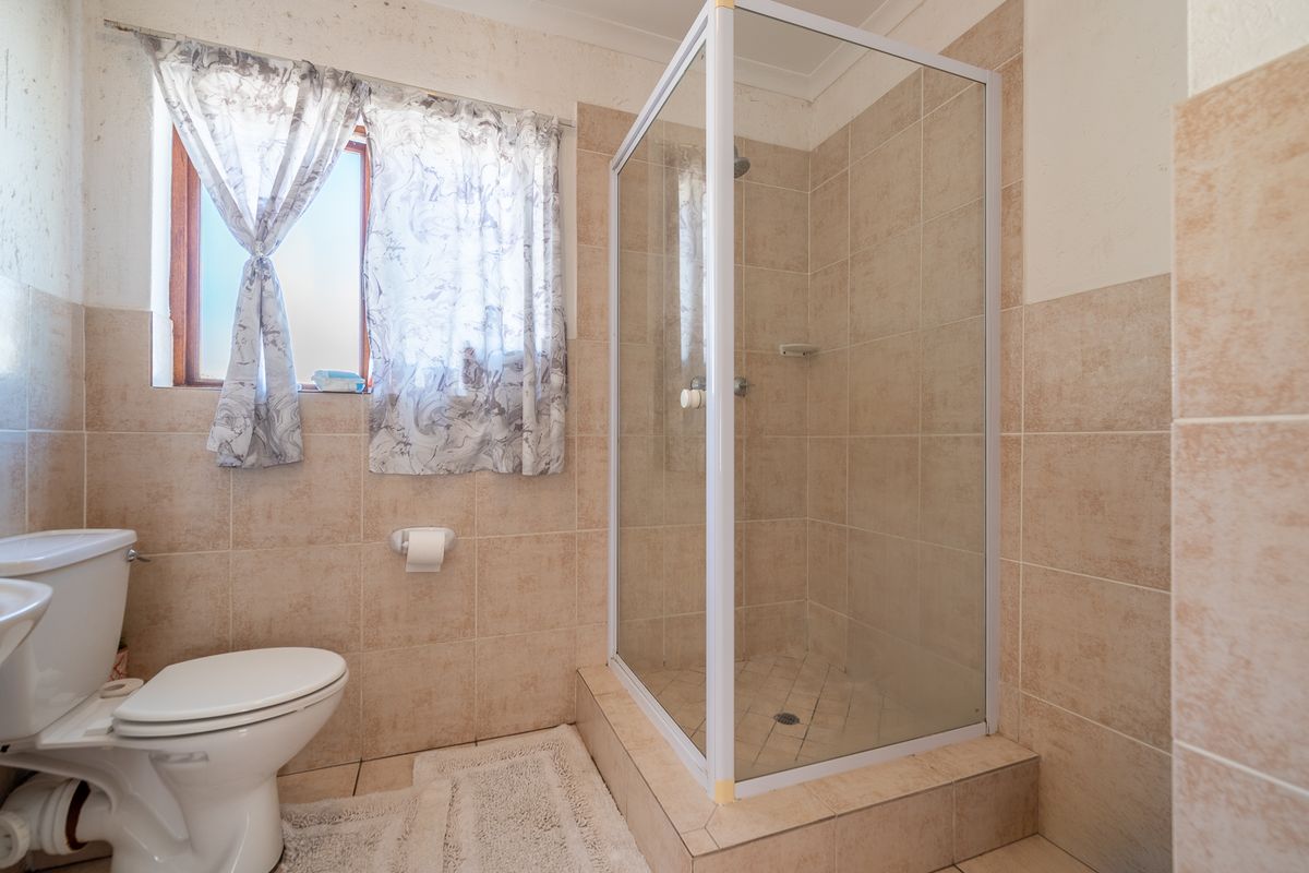 A functional bathroom featuring a glass-enclosed shower, toilet, and neutral wall tiling, offering a practical layout with natural light from the window.