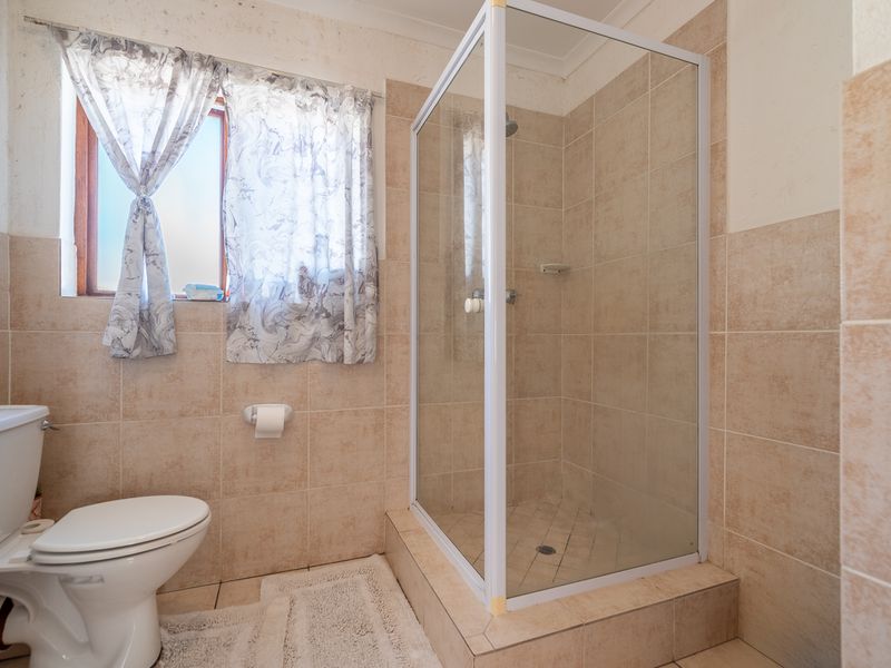 A functional bathroom featuring a glass-enclosed shower, toilet, and neutral wall tiling, offering a practical layout with natural light from the window.