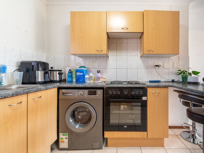 A functional kitchen featuring light wood cabinetry, granite countertops, a built-in oven, electric hob, and an integrated washing machine.