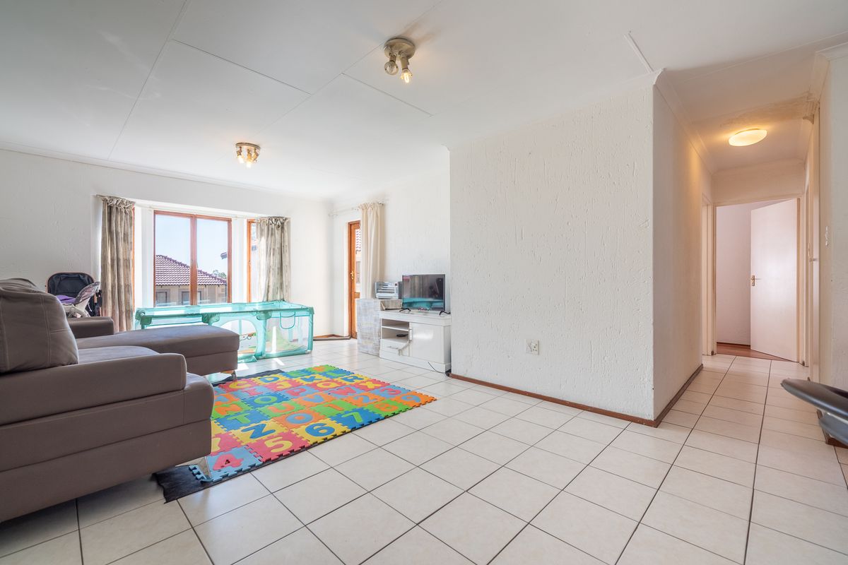 Spacious living area featuring tiled flooring, textured walls, and a bay window, providing a bright and functional space with direct access to the hallway.