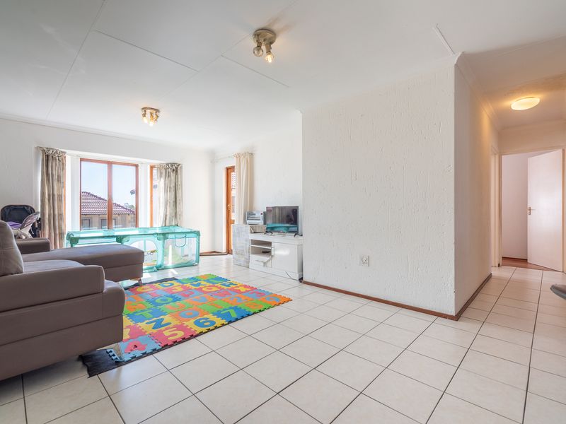 Spacious living area featuring tiled flooring, textured walls, and a bay window, providing a bright and functional space with direct access to the hallway.