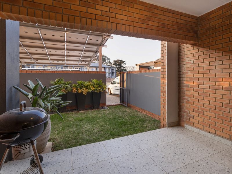 A covered patio area featuring exposed brick walls and tiled flooring, overlooking a small private garden space with a boundary wall.