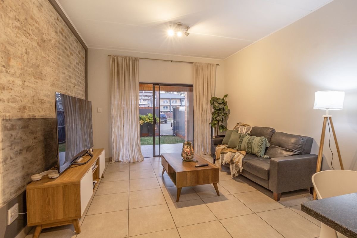 A well-maintained living room featuring an exposed brick accent wall, neutral tiled flooring, and a sliding glass door providing access to the outdoor area.