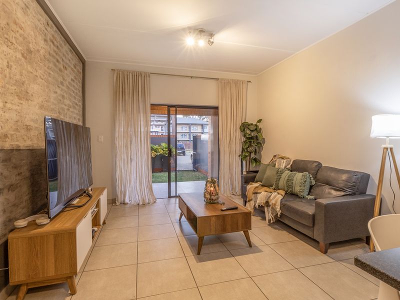 A well-maintained living room featuring an exposed brick accent wall, neutral tiled flooring, and a sliding glass door providing access to the outdoor area.