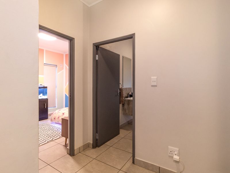A clean and well-maintained hallway featuring neutral tiled flooring, connecting to adjacent bedroom and bathroom spaces.