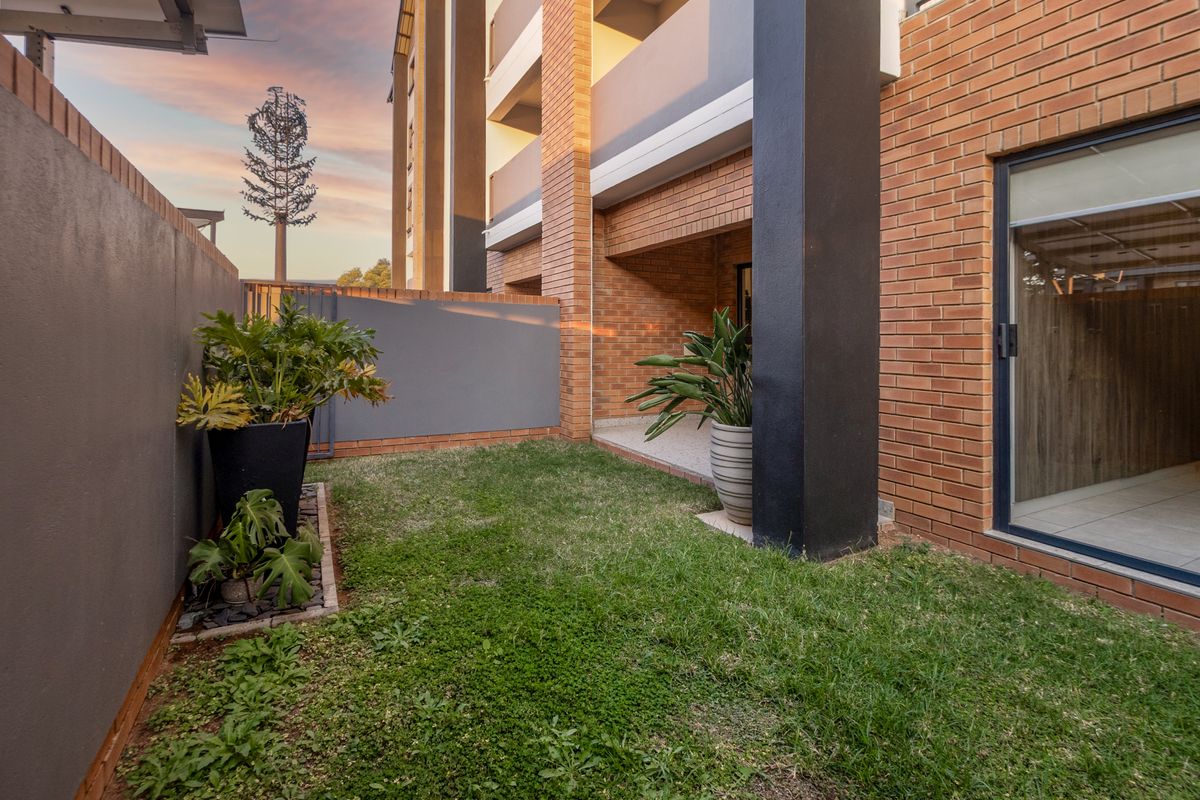 A private ground-floor garden area featuring a small lawn, paved patio section, and direct access to the apartment interior via a sliding glass door.