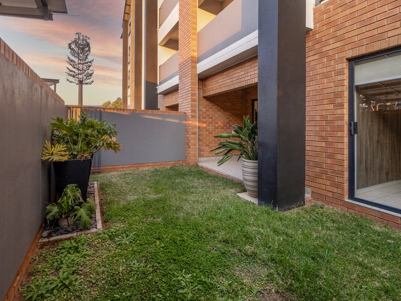 A private ground-floor garden area featuring a small lawn, paved patio section, and direct access to the apartment interior via a sliding glass door.