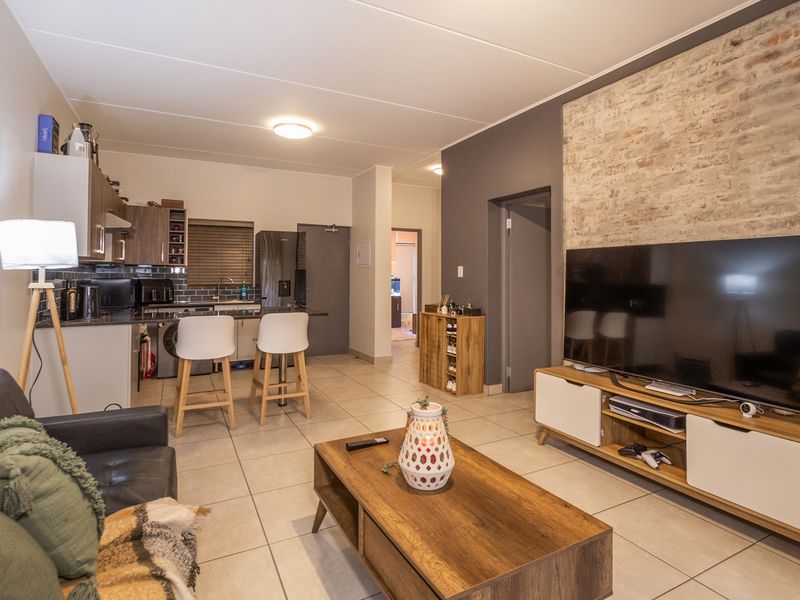 An open-plan living and kitchen area featuring a striking exposed brick feature wall, modern tiled flooring, and a functional kitchen layout.