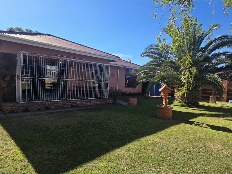 Rear view of the house featuring a lawn, established palm tree, stone-clad wall sections, and security bars on the windows.