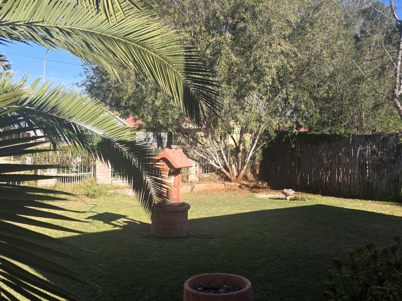 A private backyard garden featuring a manicured lawn, a decorative brick wishing well, and natural reed perimeter fencing.