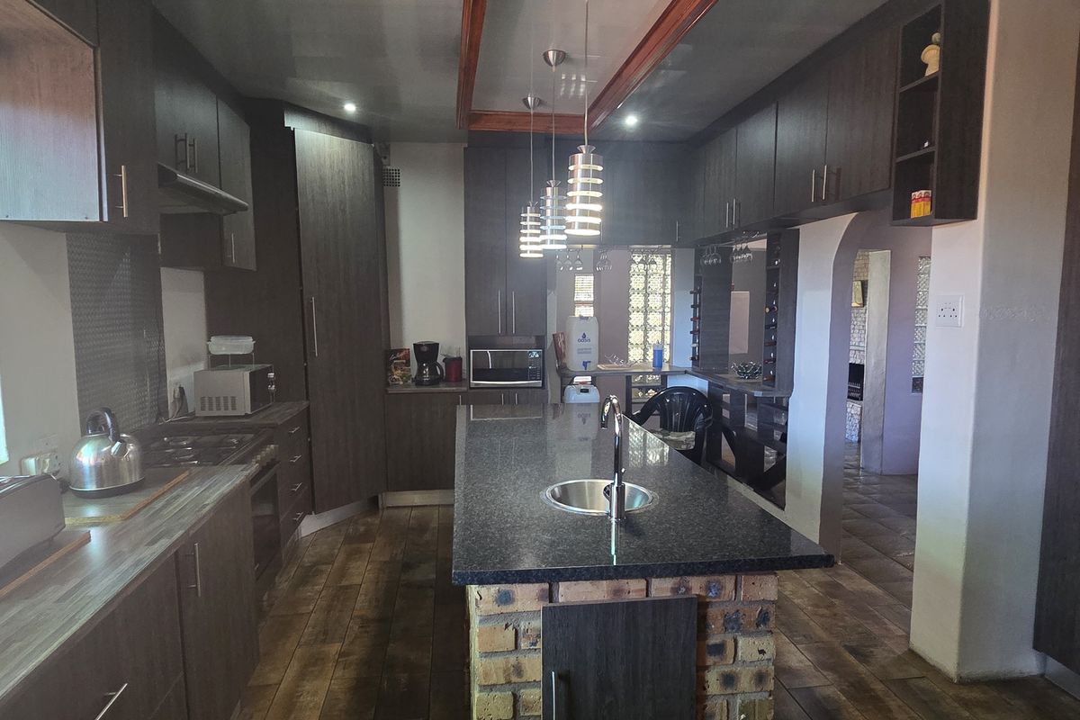 A spacious kitchen featuring dark wood cabinetry, granite countertops, a central island with a sink, and exposed brick accents.