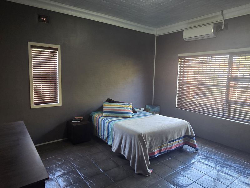 A bedroom featuring dark-toned walls, tiled flooring, fitted venetian blinds, and a wall-mounted air conditioning unit.