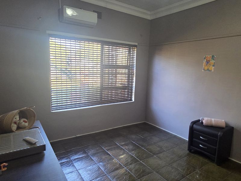 A spacious bedroom featuring tiled flooring, a split-system air conditioner, and venetian blinds, offering a neutral canvas for personalization.