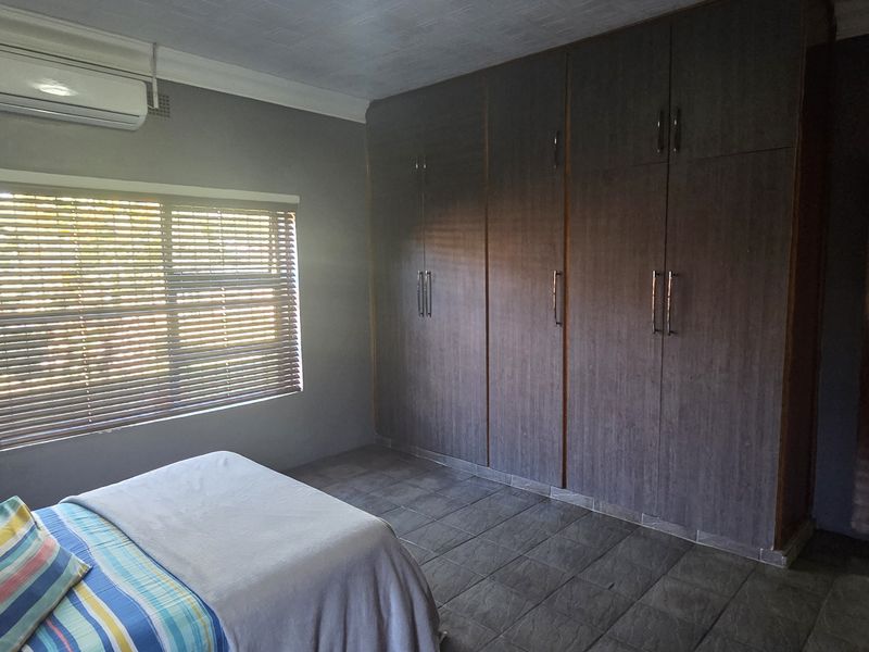 A bedroom featuring dark wood built-in cupboards, tiled flooring, and a wall-mounted air conditioning unit.