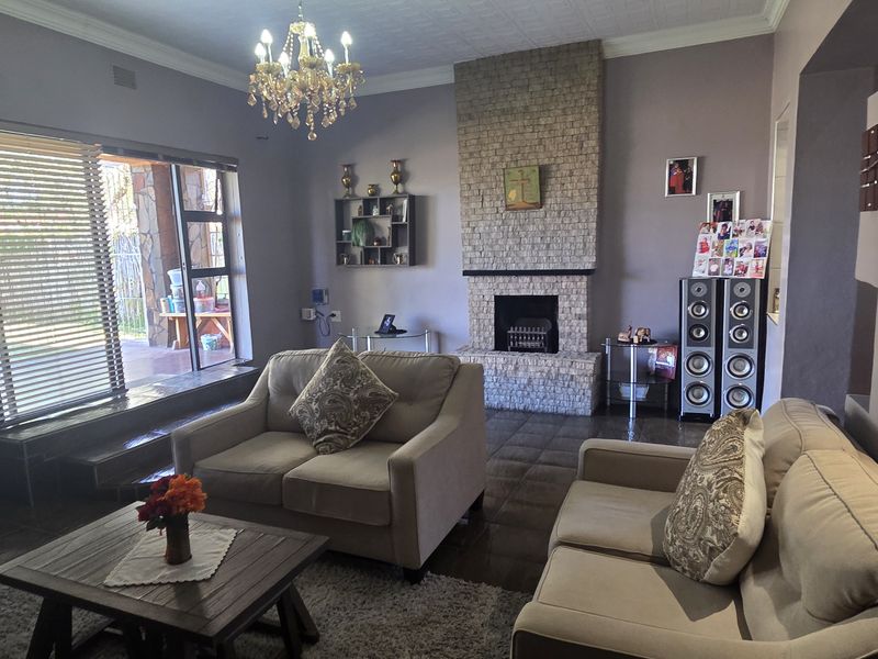 Spacious living room featuring a prominent brick fireplace, tiled flooring, and a classic chandelier, offering a comfortable and traditional atmosphere.