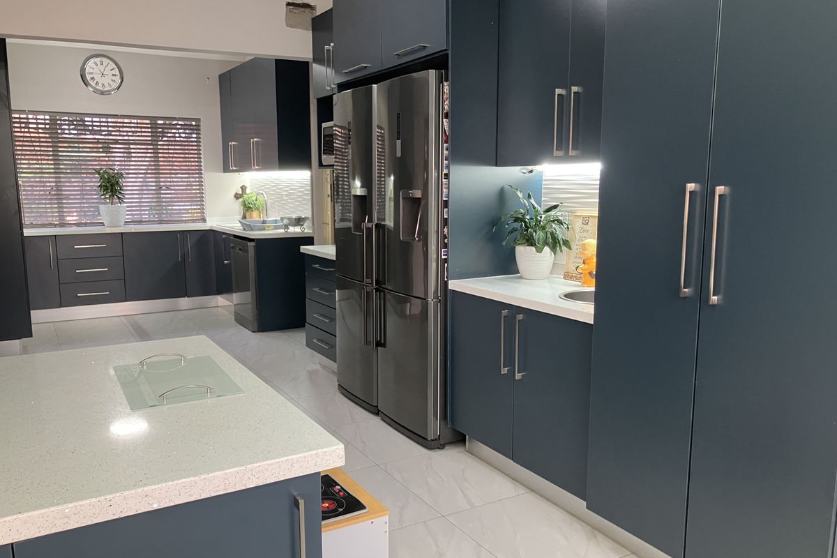 Modern kitchen featuring dark blue cabinetry, quartz countertops, integrated appliances, and tiled flooring with under-cabinet lighting.