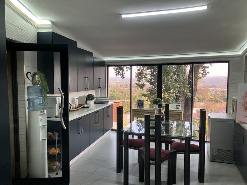 Modern open-plan kitchen and dining area featuring dark cabinetry, stone countertops, and expansive glass doors offering scenic elevated views.