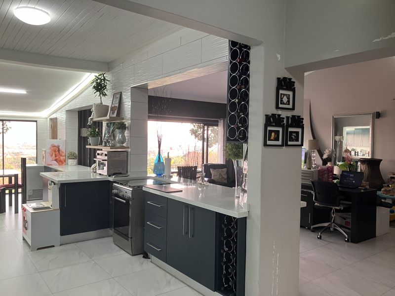 Open-plan kitchen featuring modern dark cabinetry, stone countertops, and a built-in wine rack, seamlessly flowing into the adjacent living and office areas.