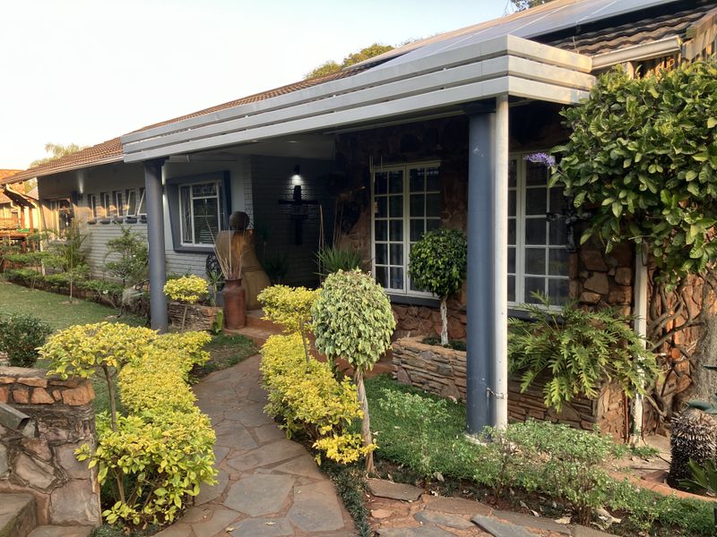 Front facade of the house featuring stone cladding, a covered patio area with metal columns, and a stone-paved walkway through a landscaped garden.