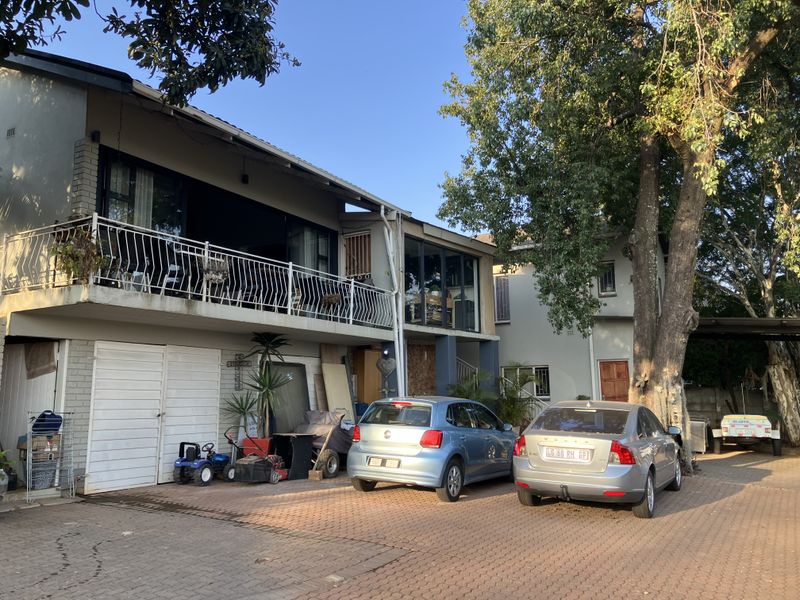 Front exterior view of a multi-level house featuring a paved driveway, garage access, and an upper-level balcony with metal railings.