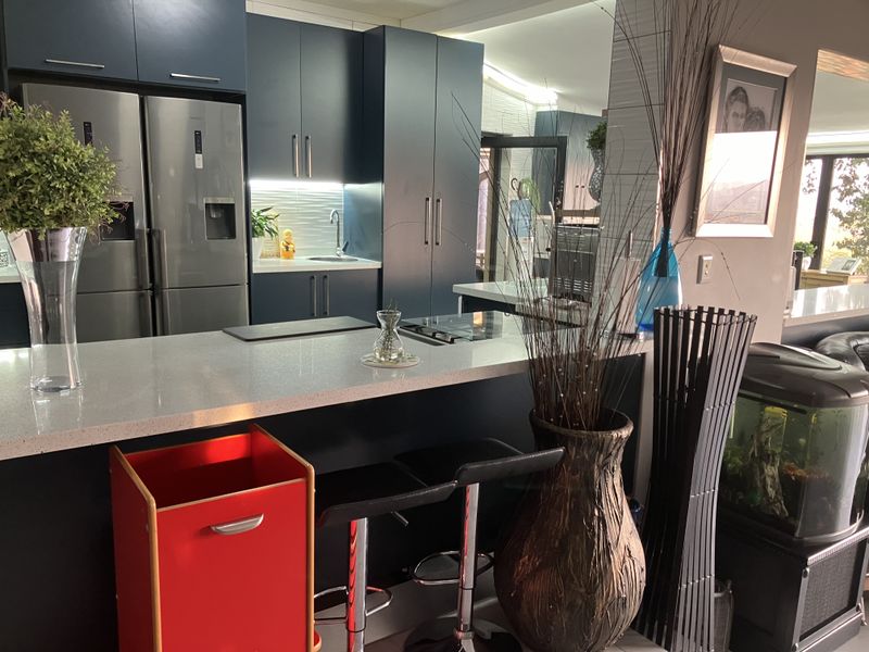 Modern kitchen featuring dark blue cabinetry, quartz countertops, and integrated cooktop with under-cabinet lighting, creating a sleek and functional culinary space.