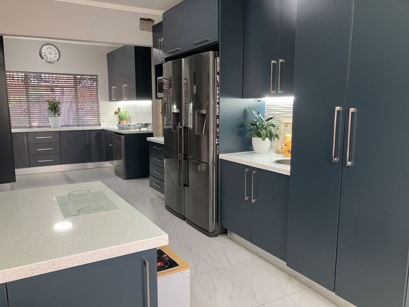 Modern kitchen featuring dark blue cabinetry, quartz countertops, integrated appliances, and tiled flooring with under-cabinet lighting.