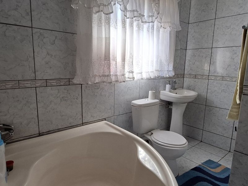 A functional bathroom featuring a pedestal washbasin, toilet, and bathtub, finished with light-toned ceramic wall and floor tiles.