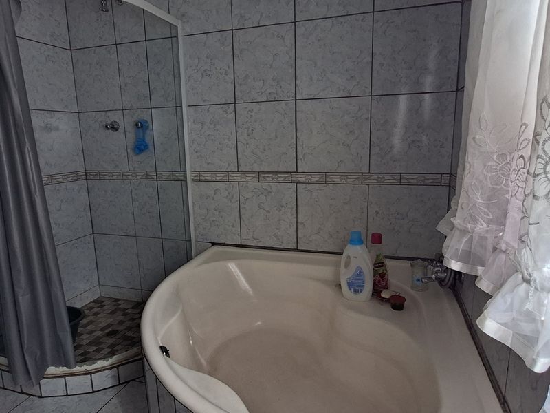 A functional bathroom featuring a built-in bathtub and a separate shower enclosure with tiled walls and flooring.