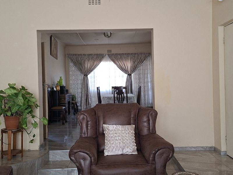A living room area featuring tiled flooring and a transition into an adjacent dining space, with neutral wall tones and standard interior finishes.