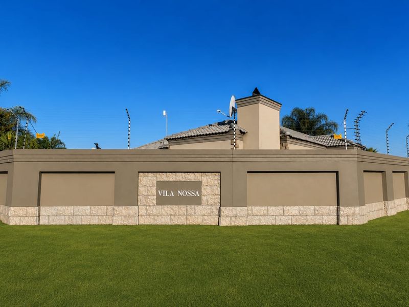 A well-maintained property exterior featuring a solid perimeter wall with stone cladding, electric fencing, and a clear view of the roofline and chimney.