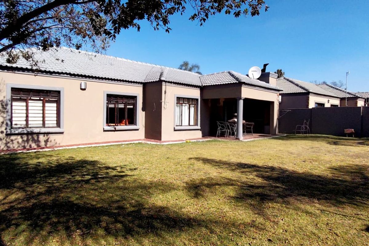 Rear view of a single-story house featuring a covered patio, tiled roof, and a spacious private garden with boundary walls.
