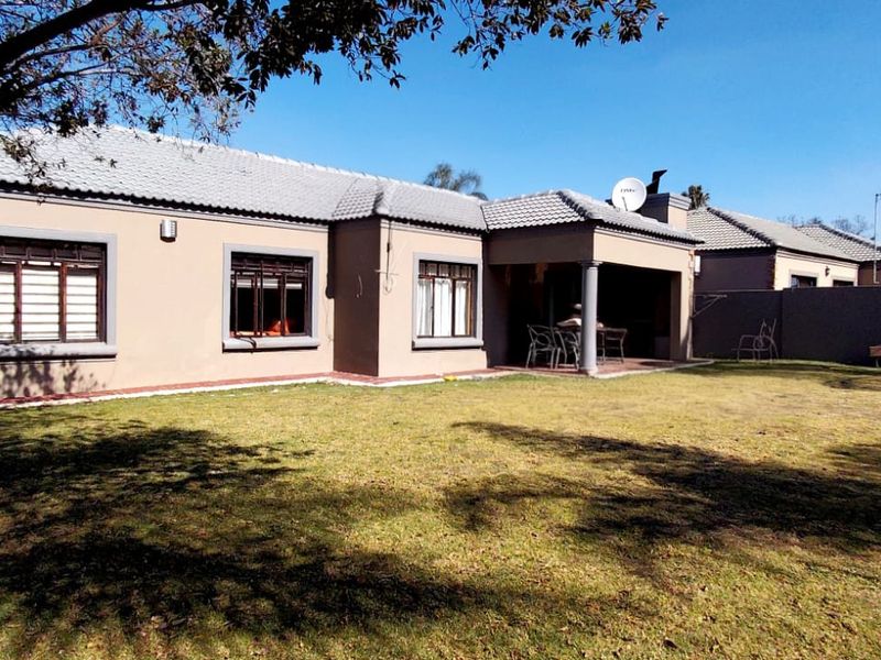 Rear view of a single-story house featuring a covered patio, tiled roof, and a spacious private garden with boundary walls.