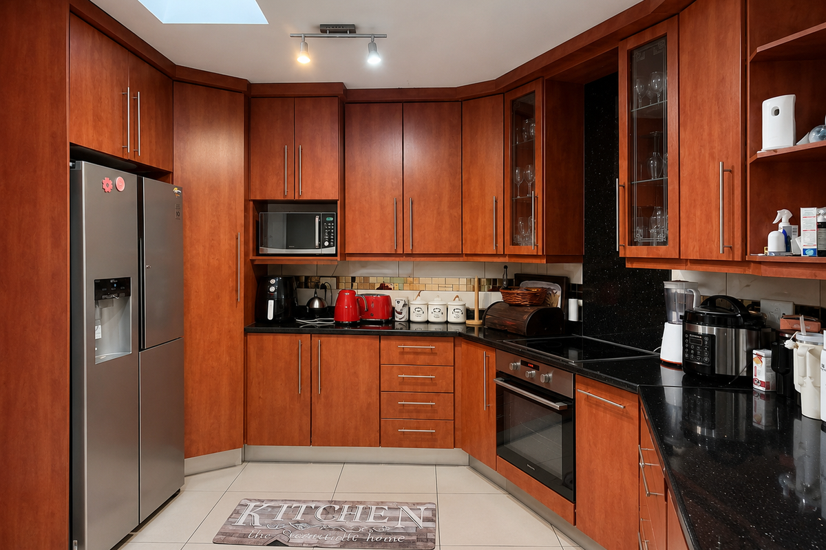 A well-maintained kitchen featuring warm-toned wooden cabinetry, black granite countertops, integrated appliances, and a skylight providing natural illumination.